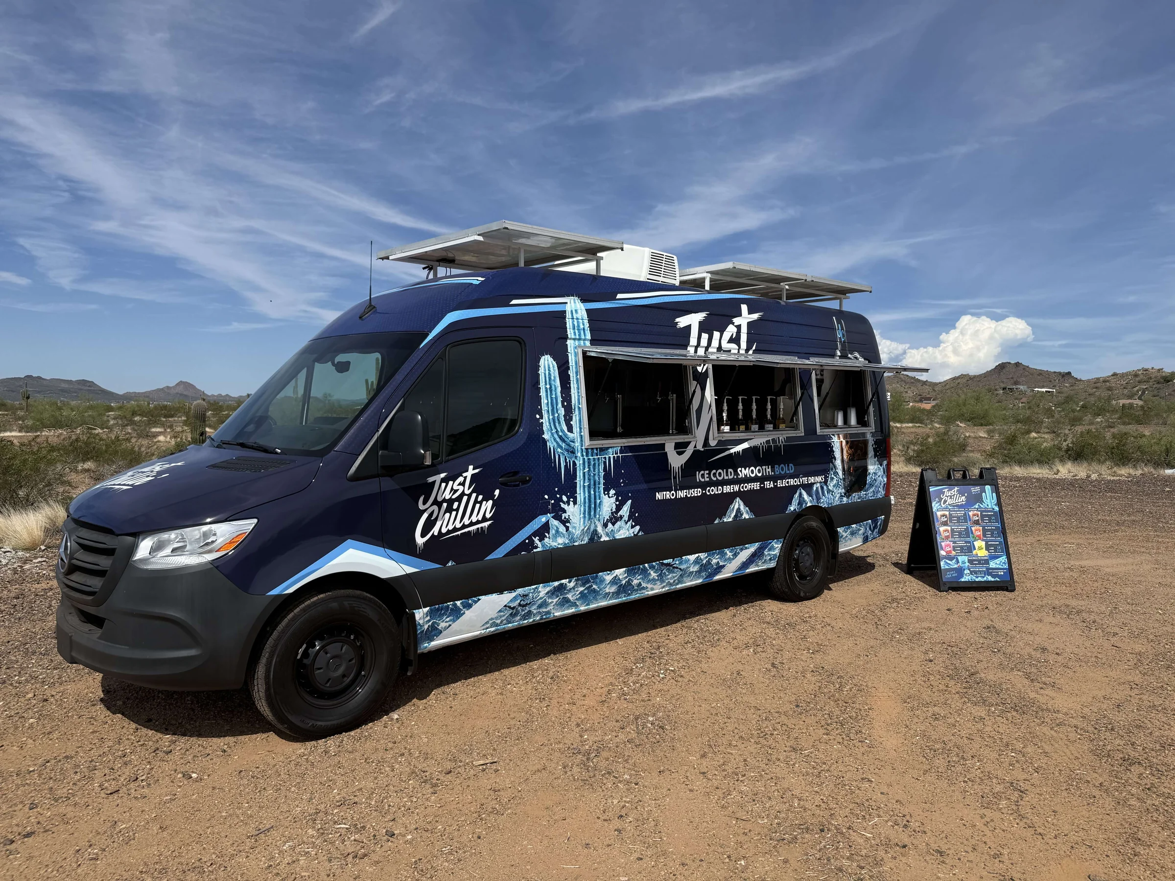 The Just Chillin' van, wrapped in navy with the icy saguaro, parked in the desert
